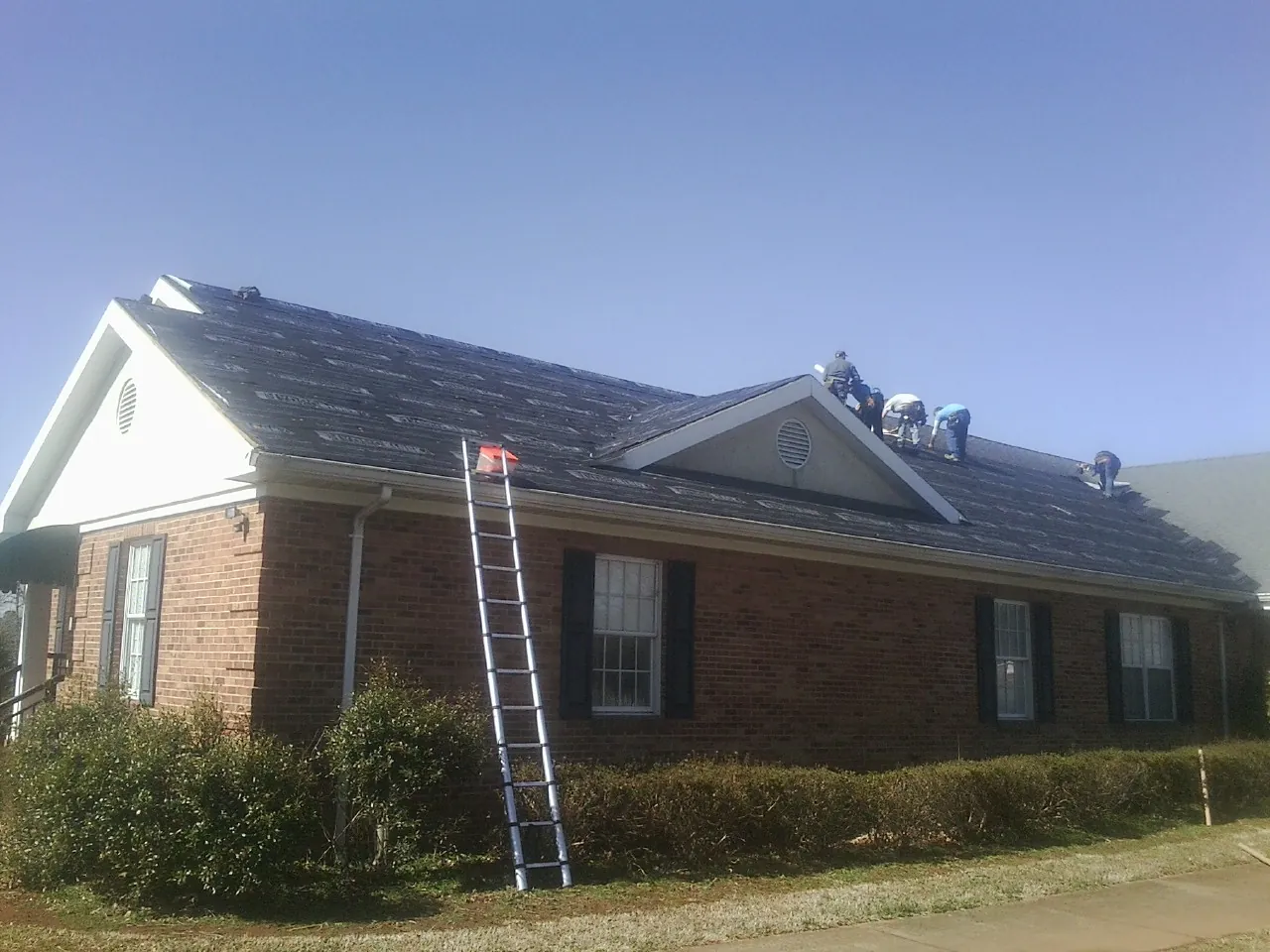 Crew tearing shingles off a brick ranch roof with a ladder set — Emergency Roof Repair work by our crew in Grindstone