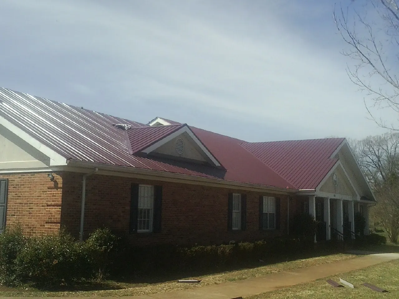 Red metal roof with gabled entries on a long brick building, from a Hail Damage Roof Repair job in Grindstone