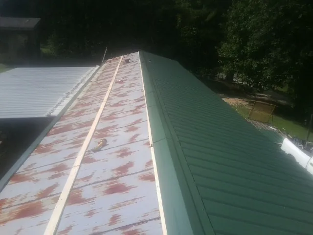 Old rusted panels beside newly installed green metal roofing — Wind Damage Roof Repair by Roofing Brothers in Grindstone