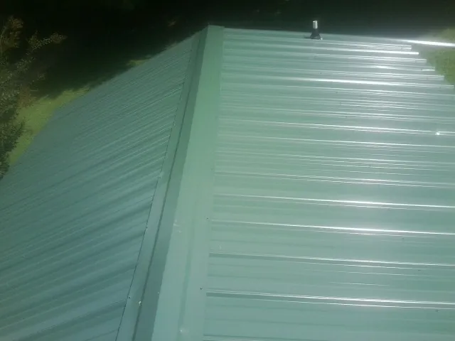 New green metal panels meeting at the ridge of a roof — Flat Roof Repair work by our crew in Grindstone