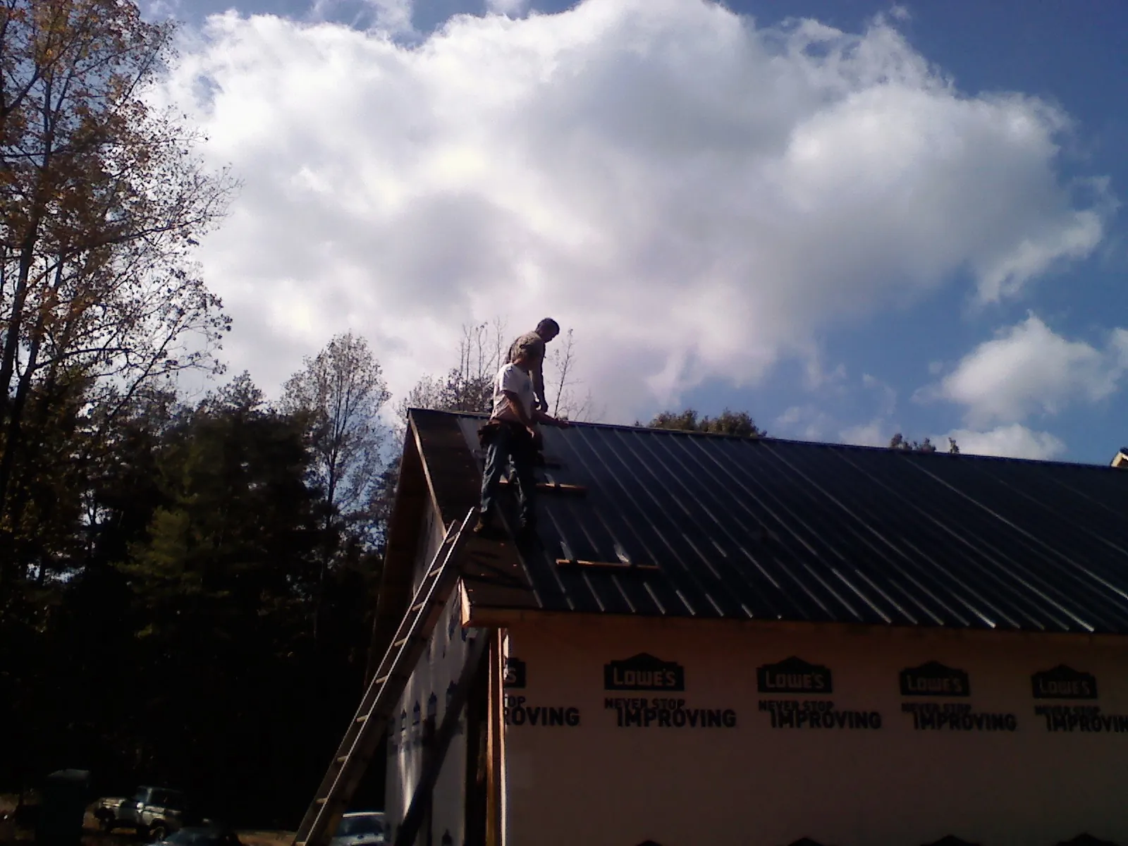 Roofer fastening dark metal panels high against a cloudy sky, from a Roof Inspection job in Grindstone