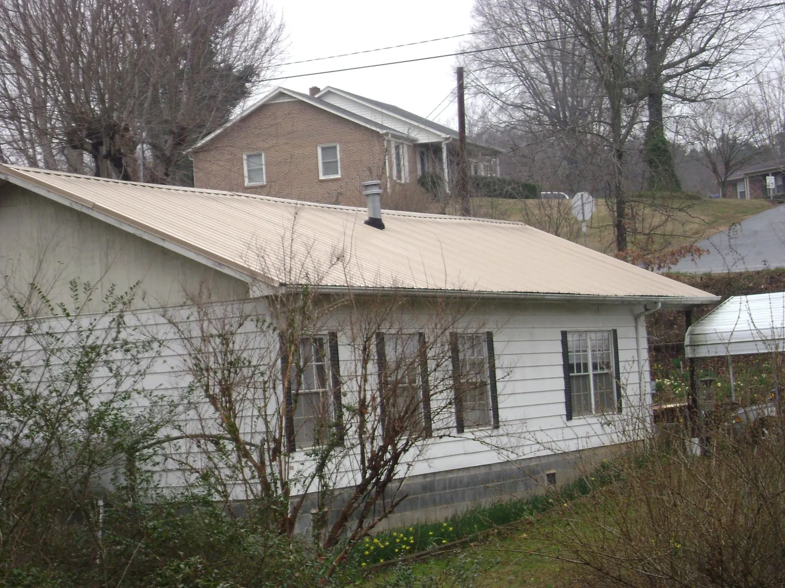 Tan metal roof on a white sided house set into a hillside — Commercial Roofing by Roofing Brothers in Grindstone